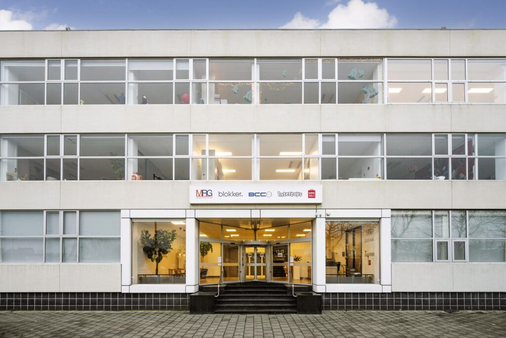 Vooraanzicht van een kantoorgebouw aan de Van der Madeweg met logo’s van MRG, Blokker, BCC, Intertoys en MINISO boven de entree.